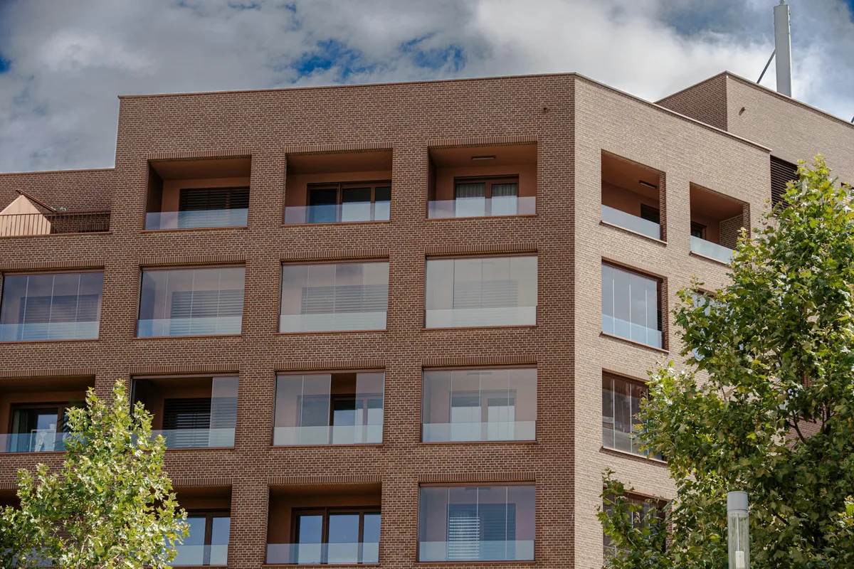 A modern brick apartment building with glazed balconies and trees in front